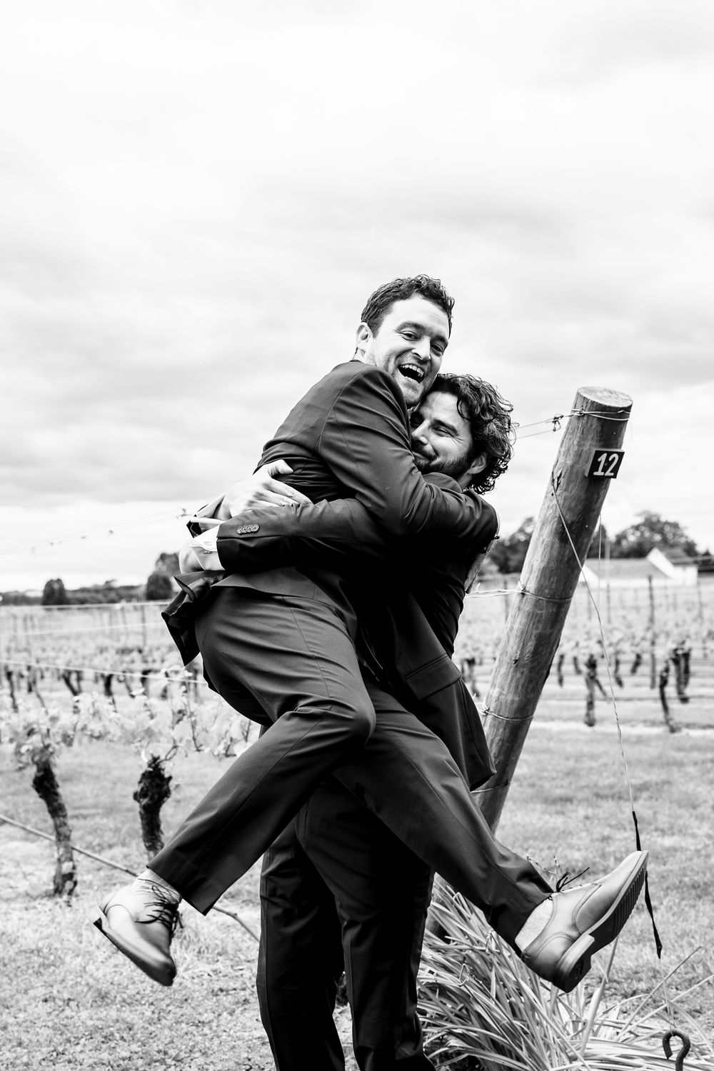Playful wedding couple embracing and laughing in a vineyard setting.