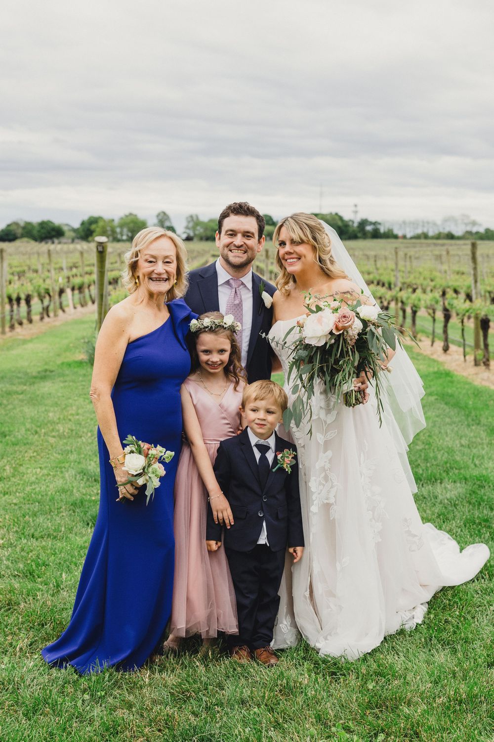 Wedding party in blue and pink dresses posing together in vineyard.