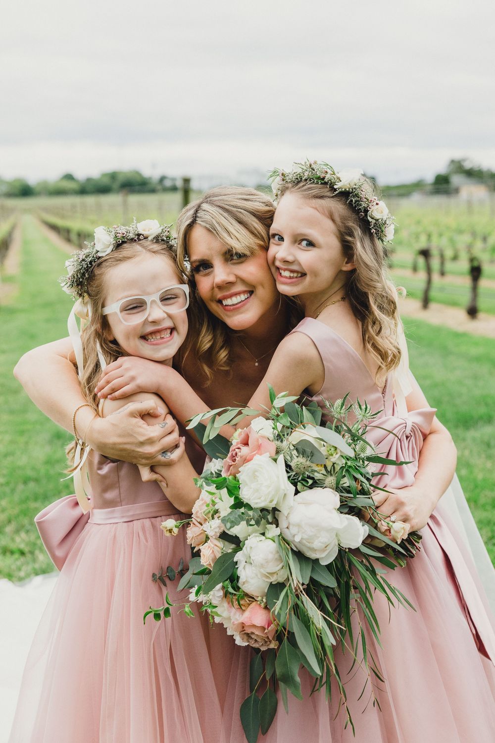 Bridesmaids in blush pink dresses share a joyful moment while holding elegant white floral bouquets.