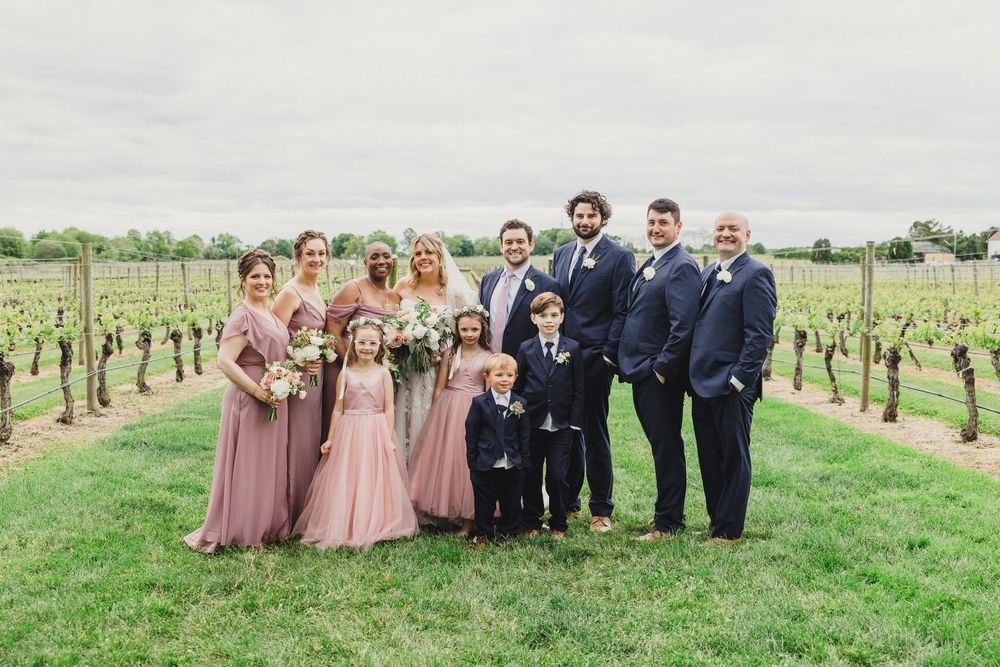 Wedding party poses together in rows among vineyard rows on a bright spring day.