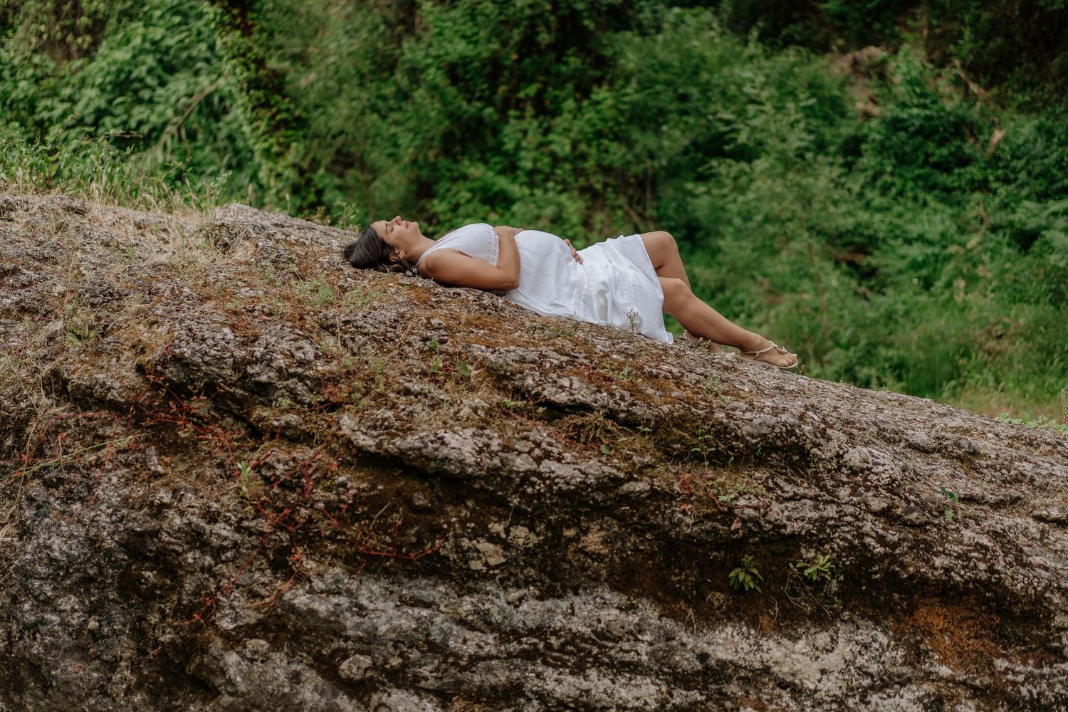 A person in a red shirt walks on a fallen tree trunk in a lush green forest setting.