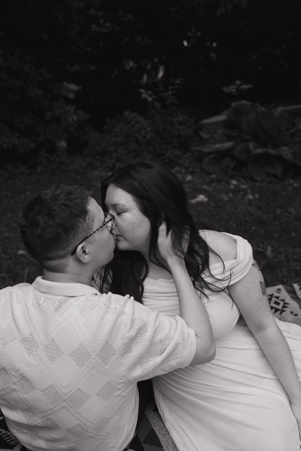 Intimate black and white photo of a couple sharing a tender moment outdoors.