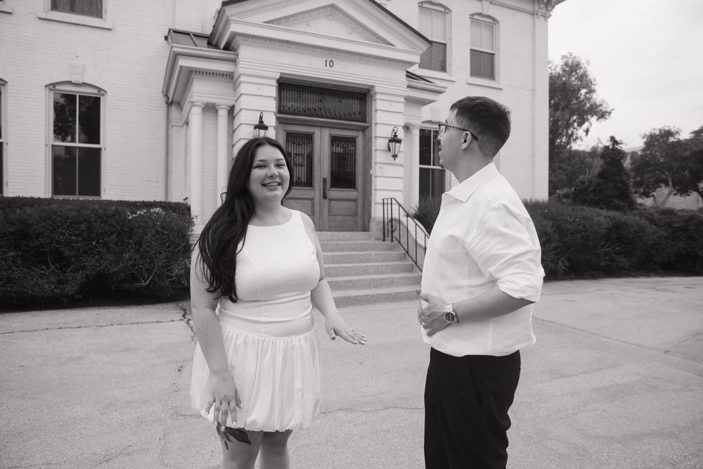 A couple shares a romantic moment in front of a white classical building with columns and windows.