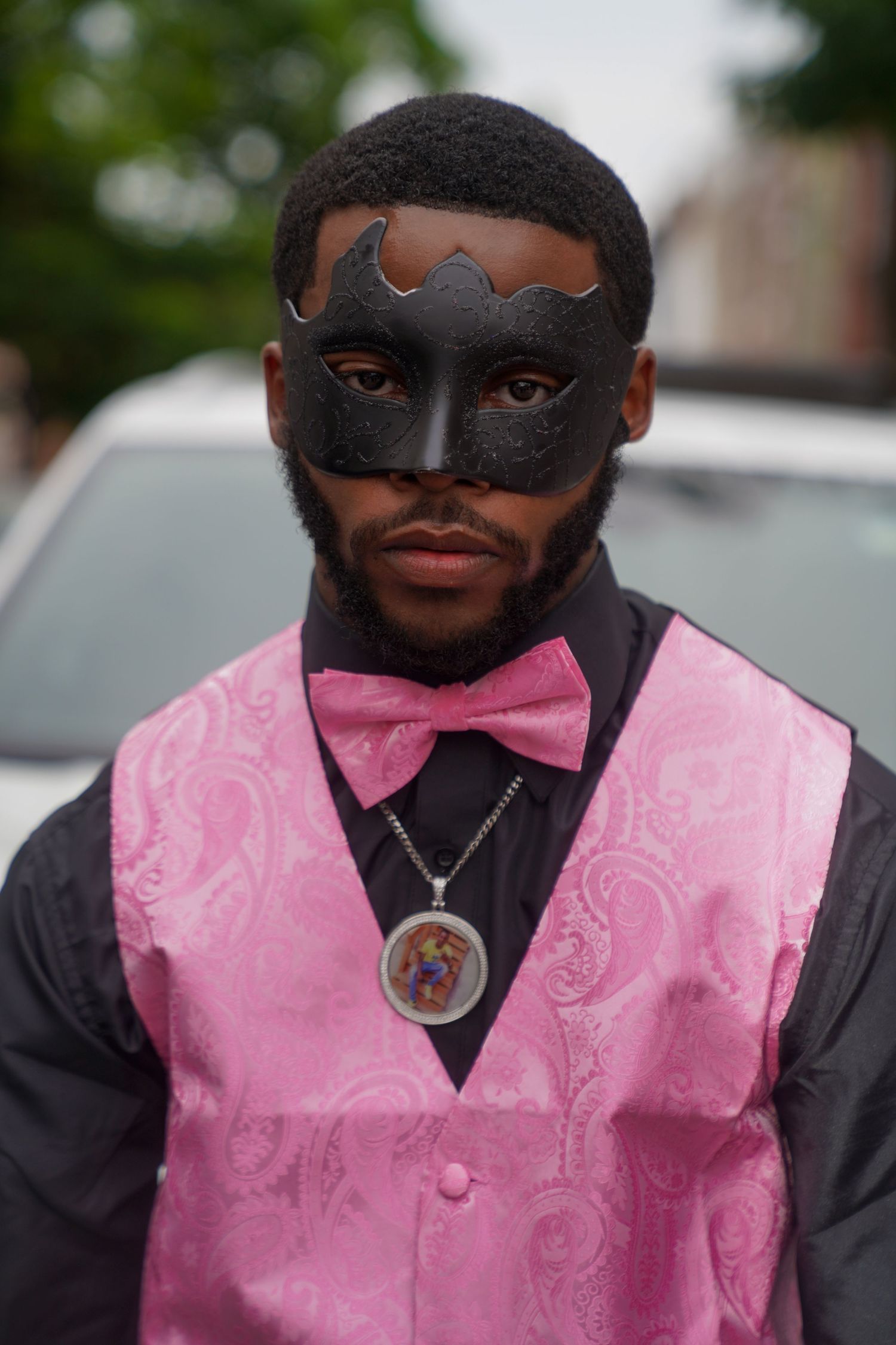 Person wearing a black mask and pink paisley vest with black dress shirt.