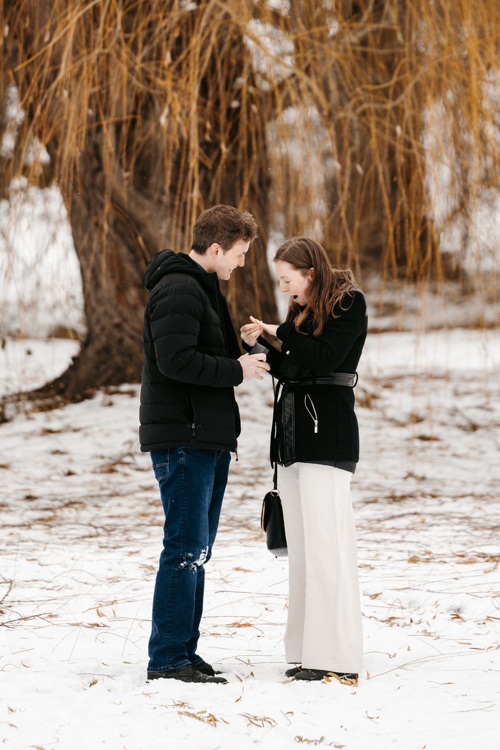 A couple shares an intimate moment in a snowy winter landscape with golden trees in the background.