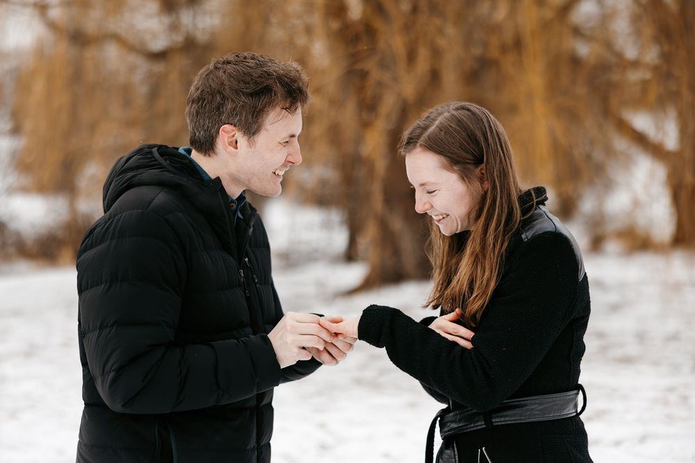 A couple in winter coats shares a romantic moment together in the snow during an engagement photoshoot.
