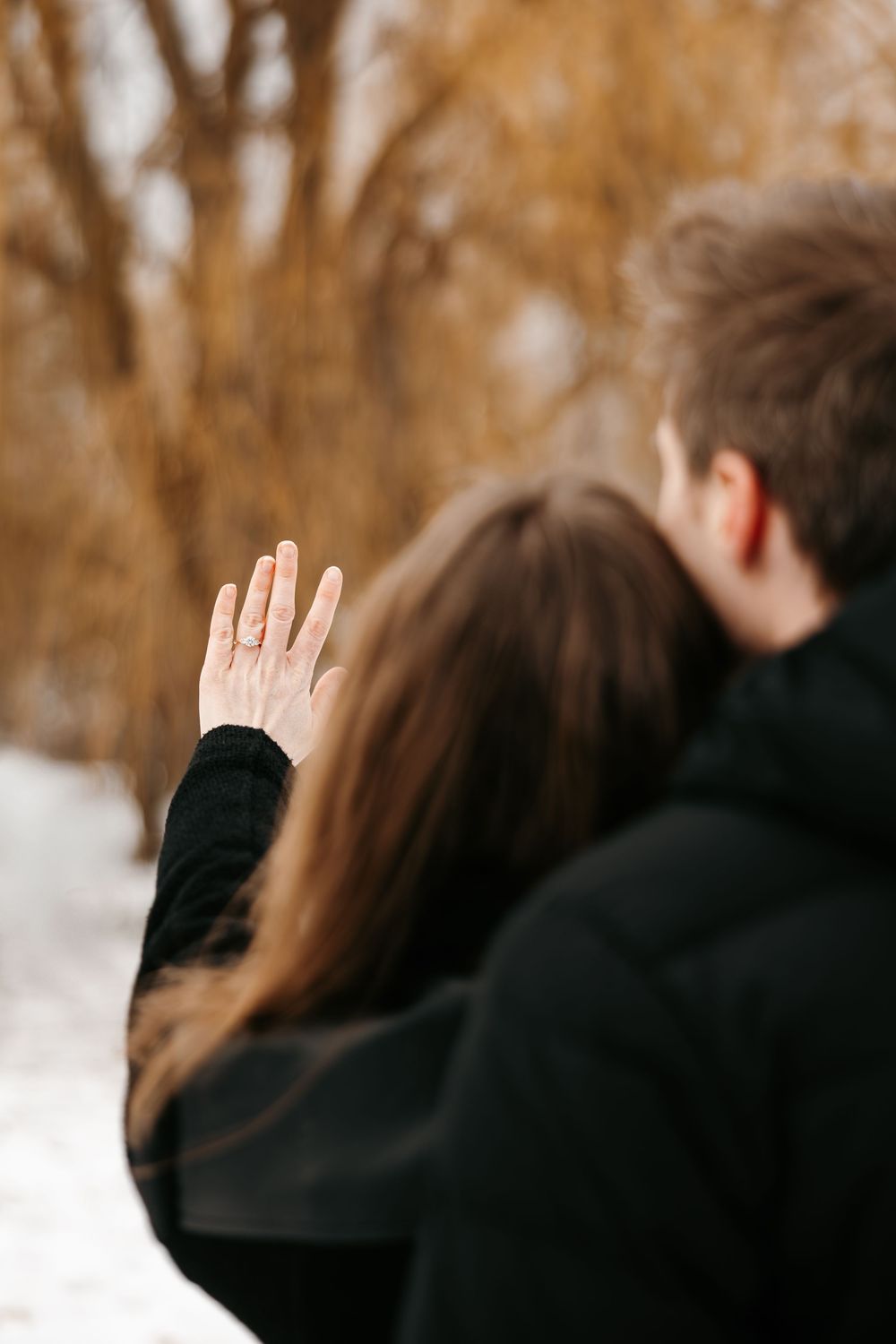 A couple embracing in a snowy winter scene with golden autumn trees in the background.