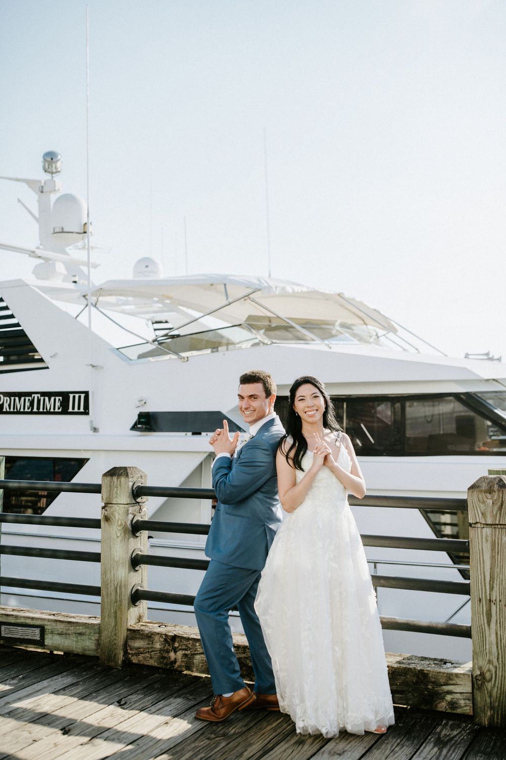 A couple shares playful moments at a marina dock with boats and yachts in the background.
