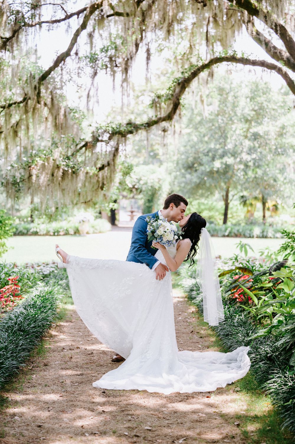Romantic wedding scene under Spanish moss-draped trees with a flowing white dress on a garden path.