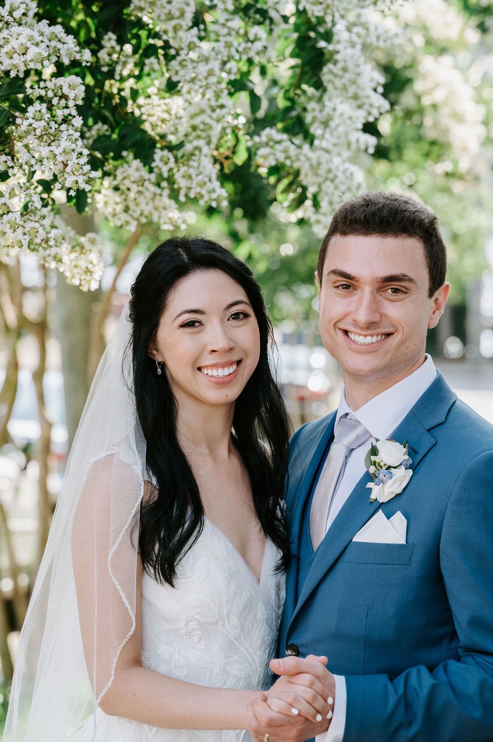 A couple shares a joyful moment under blooming white flowers on their wedding day.