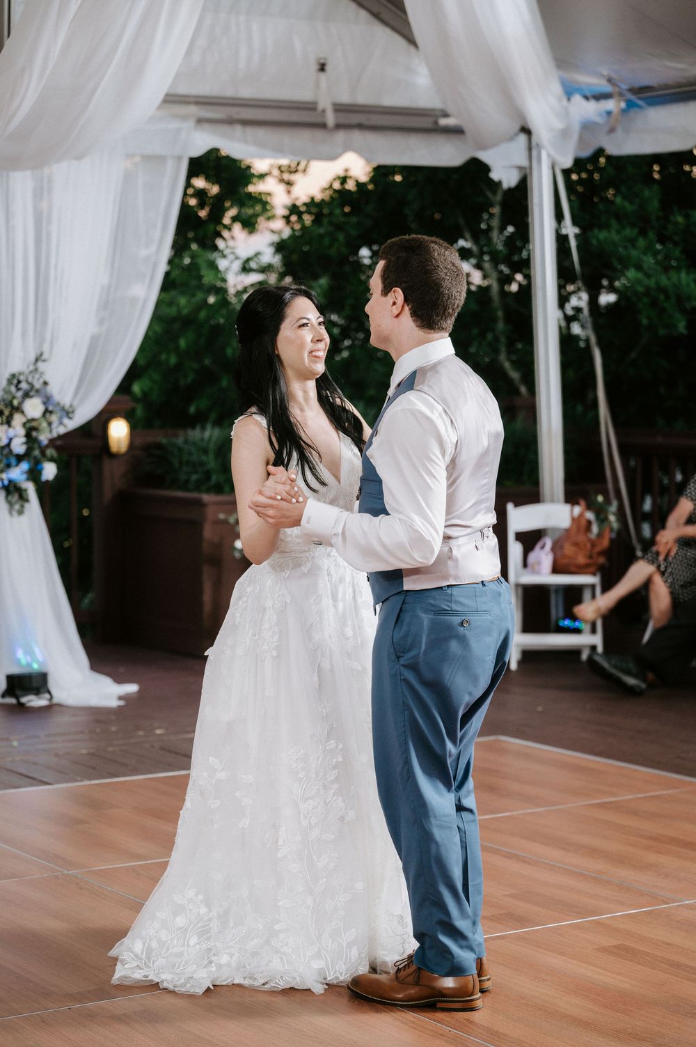 A couple shares their first dance under white draping at an outdoor wedding reception.