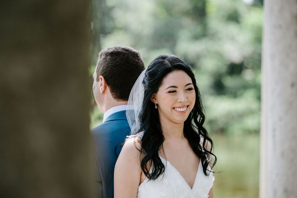 A wedding couple stands together in an outdoor garden setting surrounded by greenery.