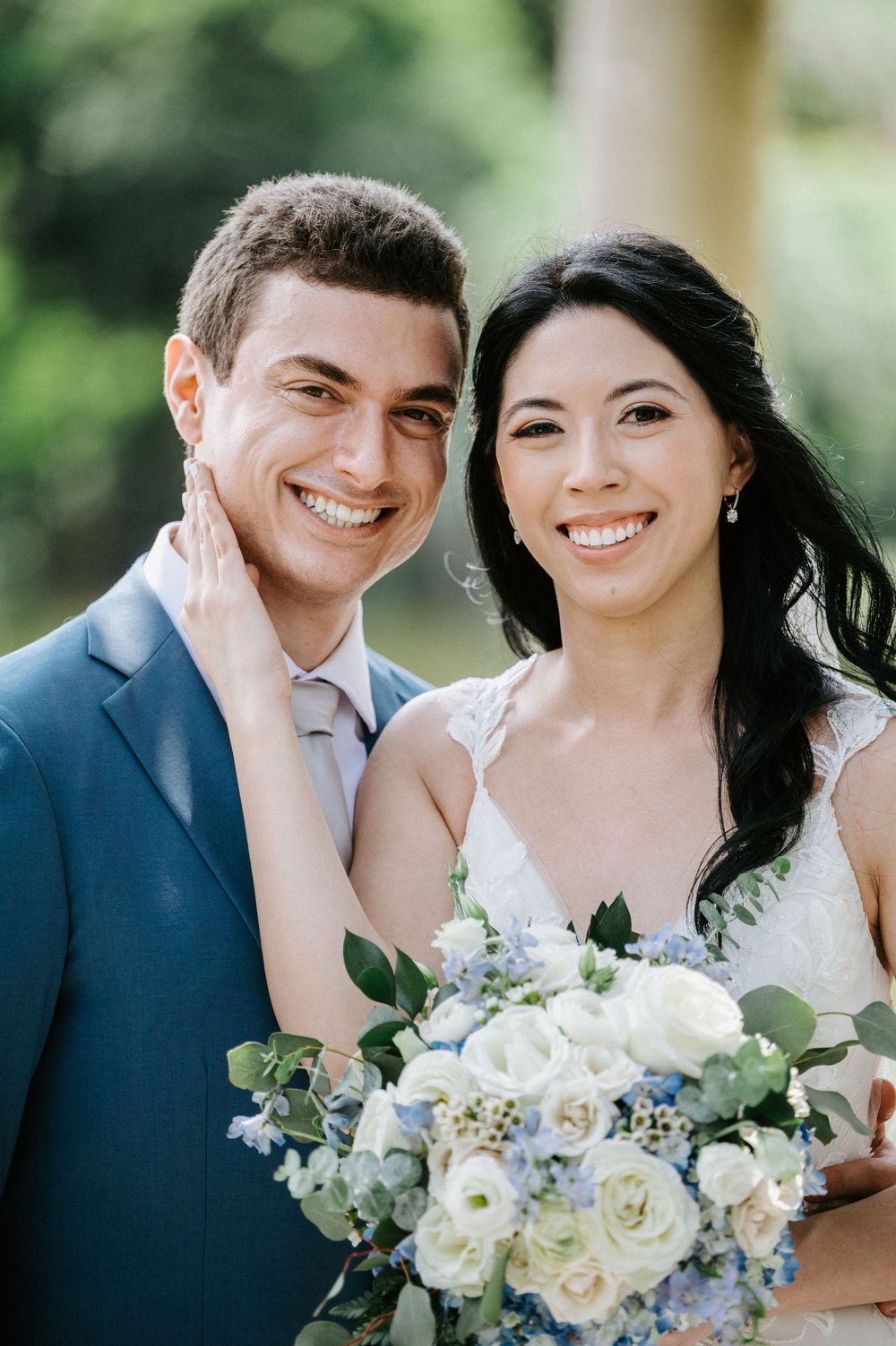 A happy couple on their wedding day with a beautiful white and blue floral bouquet.
