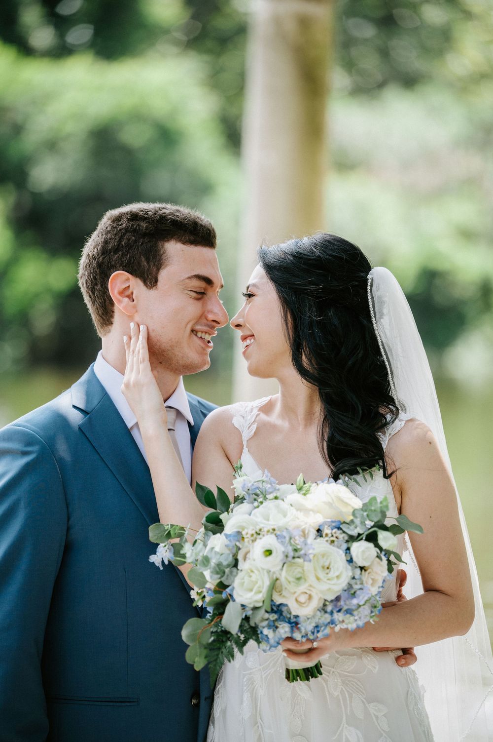 A romantic wedding couple shares intimate moments in a garden setting with white floral bouquet and navy suit.