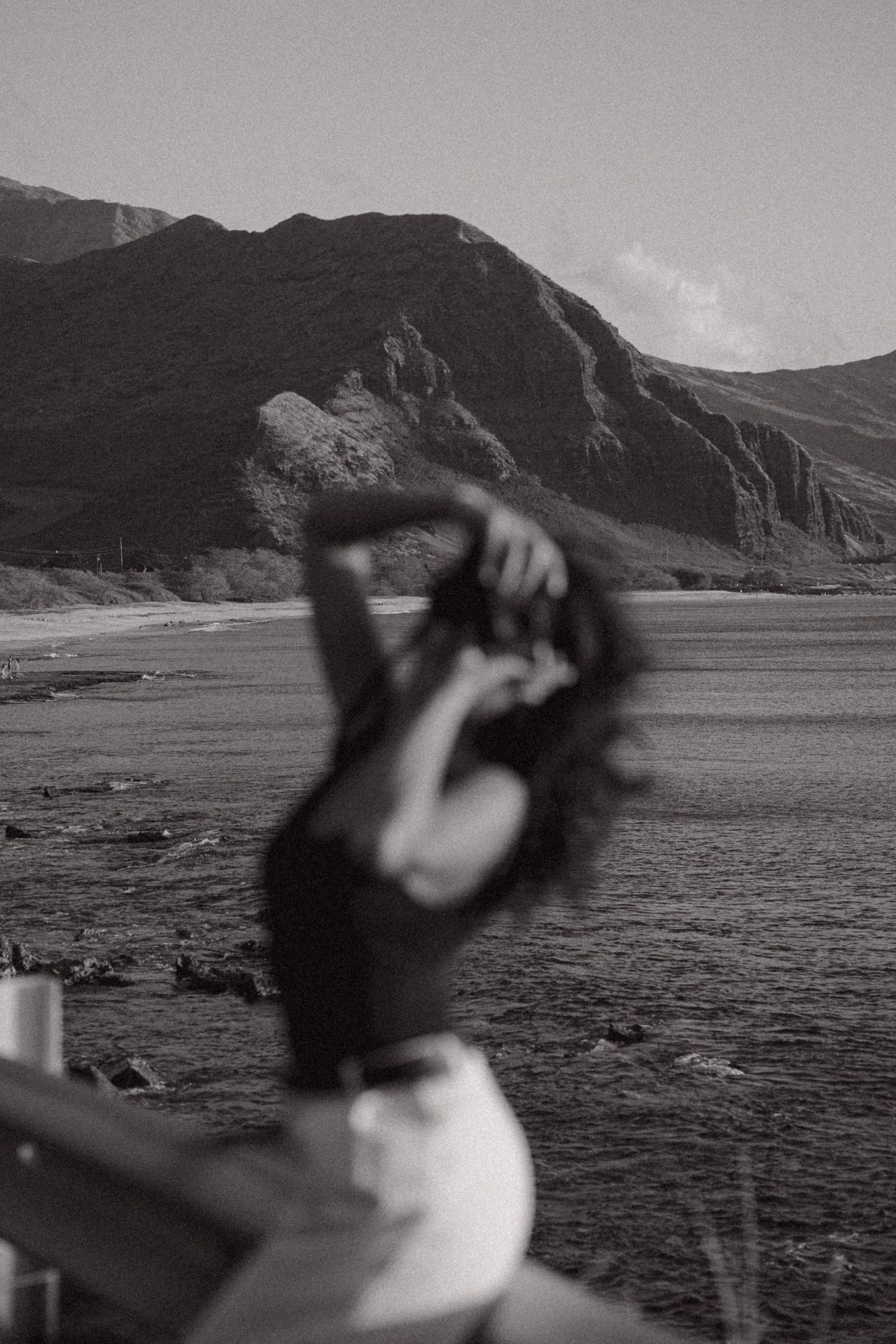 Person sits thoughtfully on a black chair against rugged coastal cliffs and sandy beach backdrop.