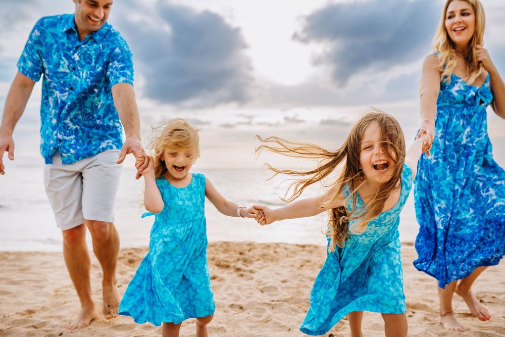 Family wearing matching blue tropical print outfits holds hands while walking on a beach at sunset.