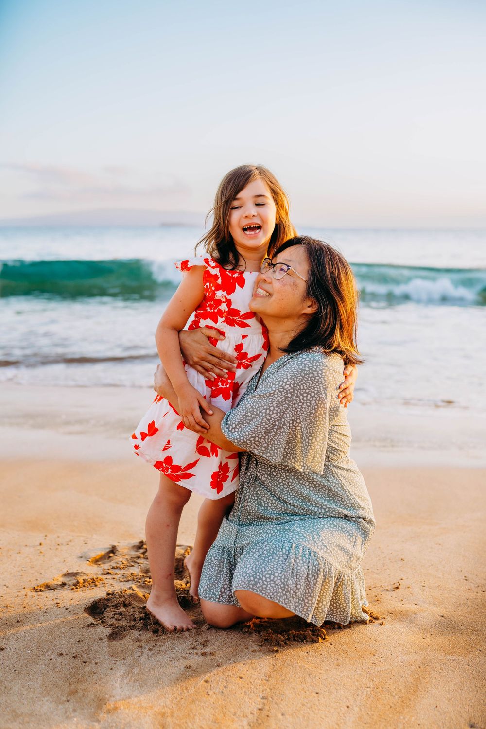 Two people share a tender moment while sitting together on a sandy beach at sunset.