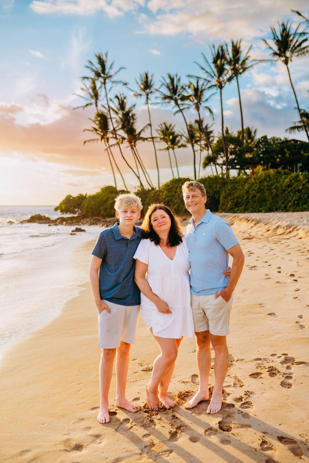 A family walks along a scenic tropical beach with palm trees and golden sand at sunset in Hawaii.