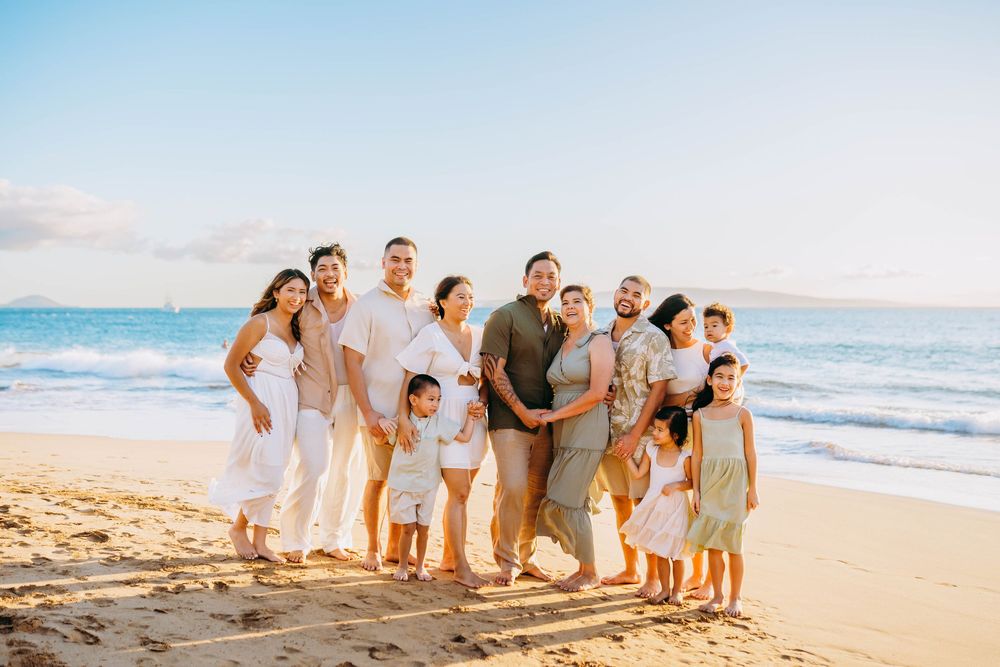 A group in coordinated white and beige outfits poses together on a sunny beach at sunset.