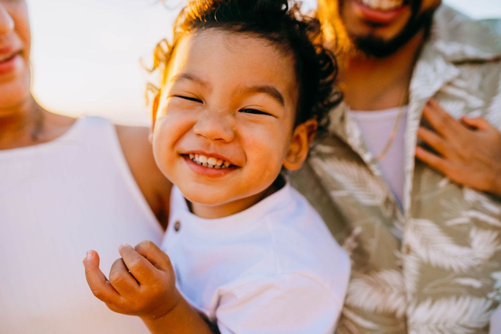 A joyful child in a white shirt laughs with pure delight during a sunny outdoor moment.