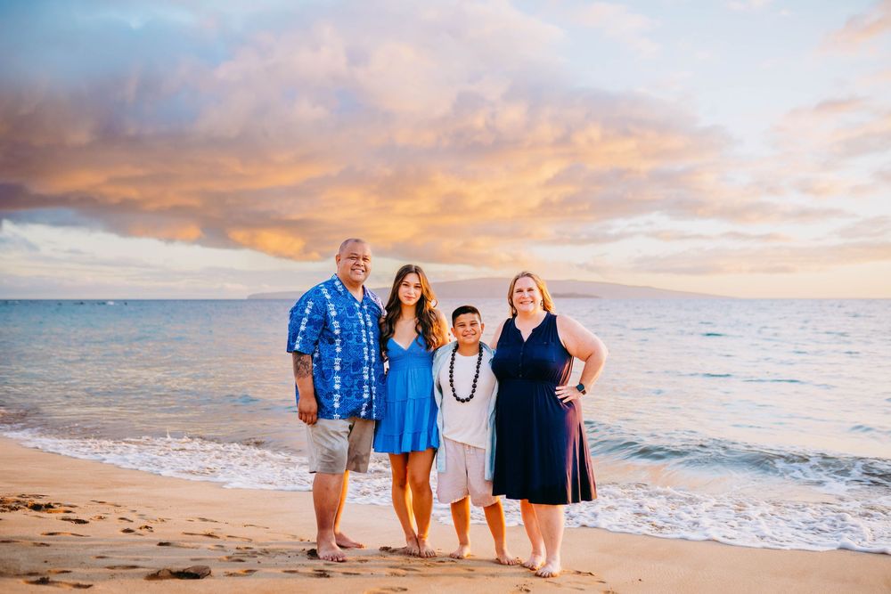 A group poses for family beach photos at sunset wearing coordinated blue outfits on a sandy shoreline.