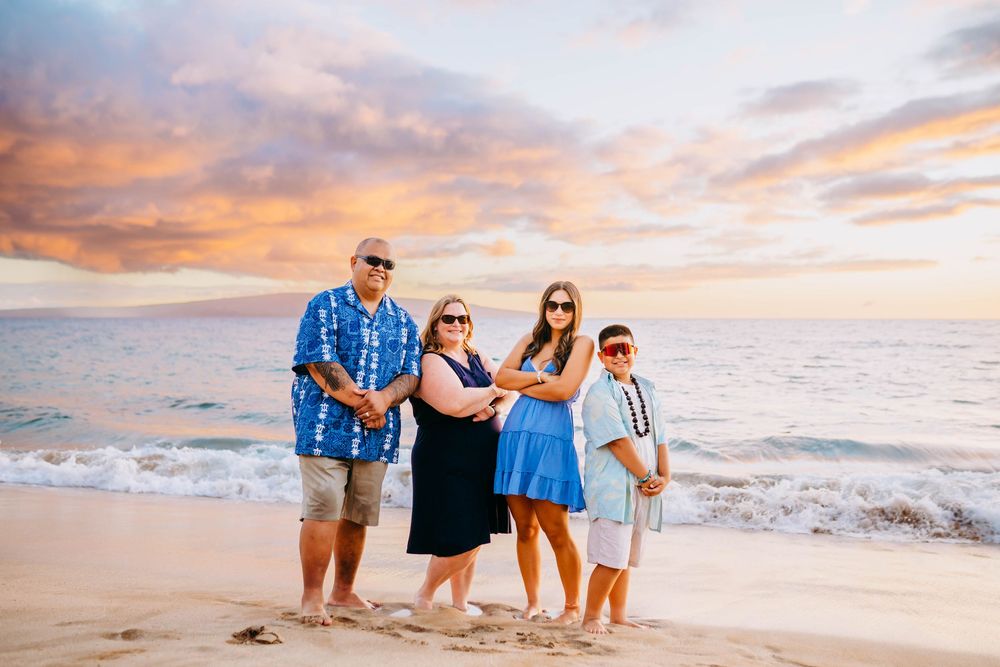 Family group poses together on sandy beach during golden sunset while wearing coordinated blue and white outfits.