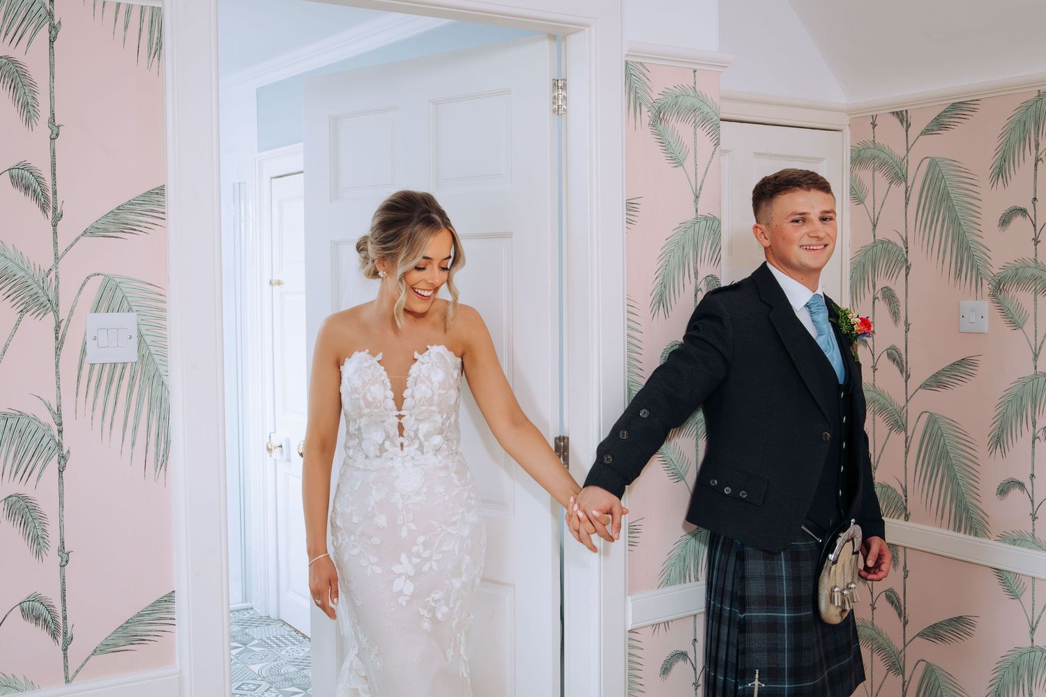A bride and groom share a tender moment in a room with tropical palm leaf wallpaper.