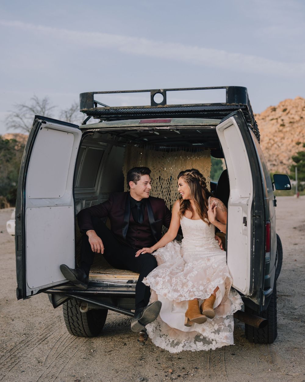 Bride and groom sit together in the back of a vintage van in a desert wedding setting.