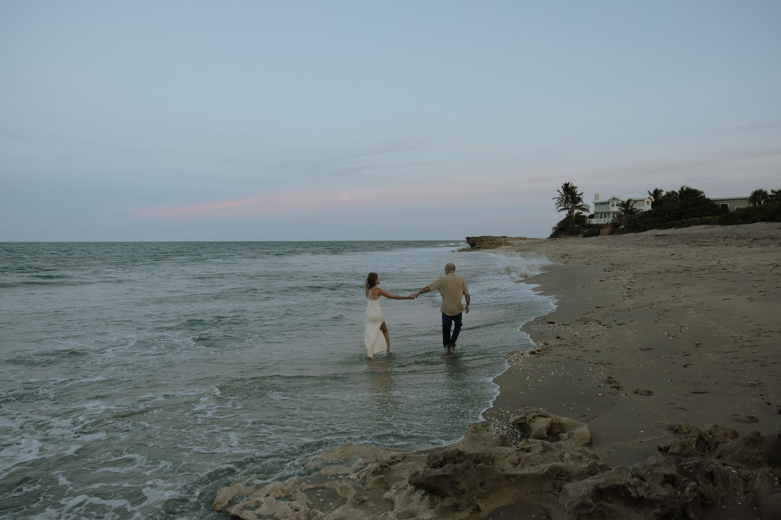 People enjoying a peaceful evening stroll along a sandy beach shoreline at sunset.