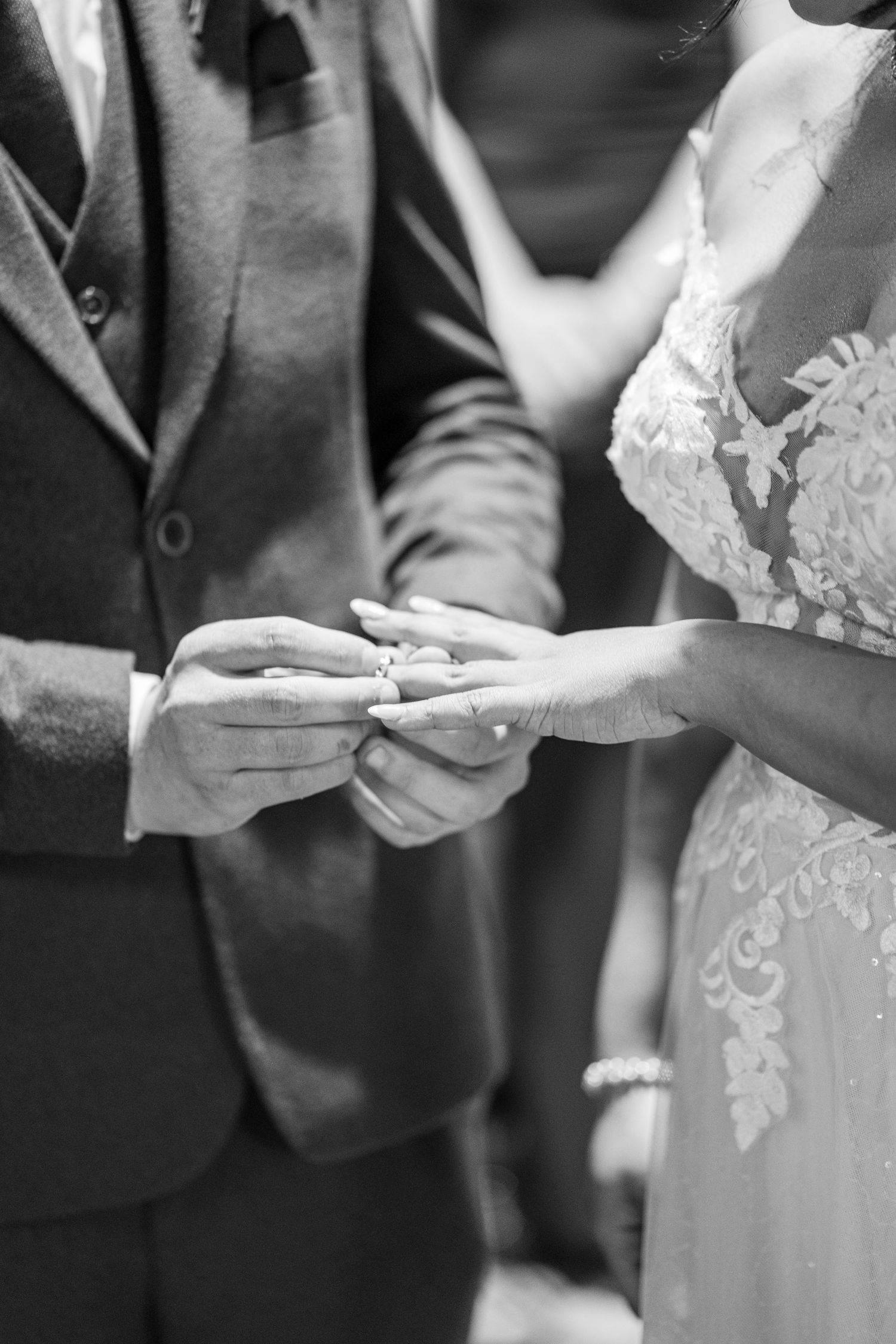 Close-up black and white photo of hands exchanging wedding rings during a ceremony.