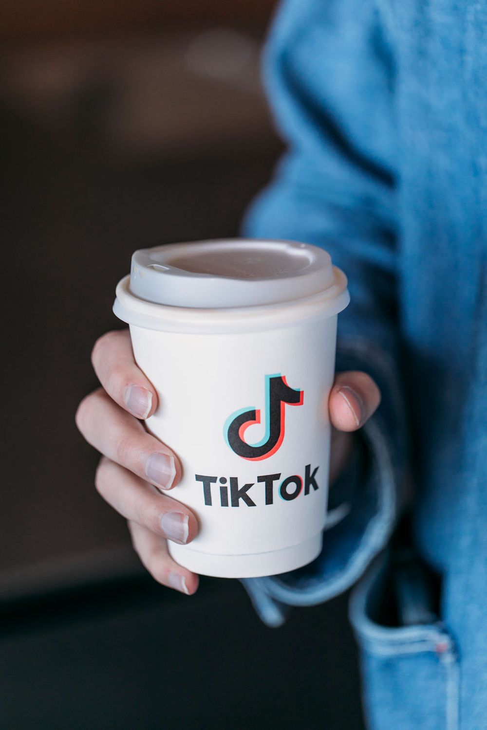 Hand holding a white coffee cup with TikTok logo and branding against a dark background.