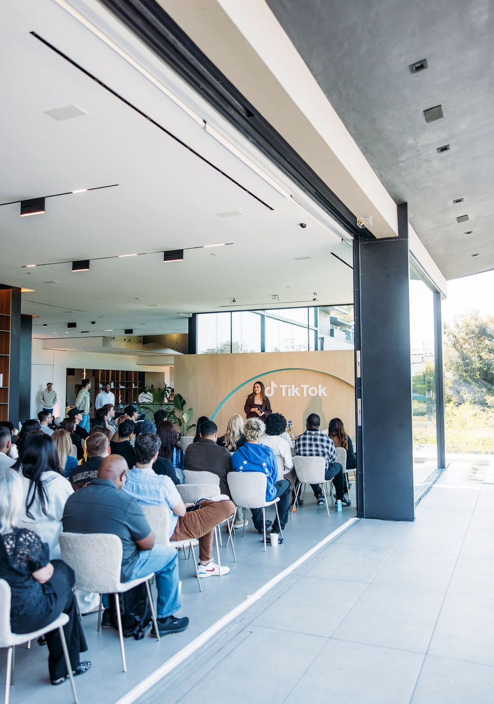 Panoramic view of a modern office space with people seated in chairs along a windowed wall.