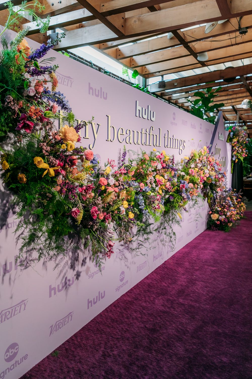 Elegant floral wall installation with purple carpet features colorful blooms against white backdrop at Hulu event.