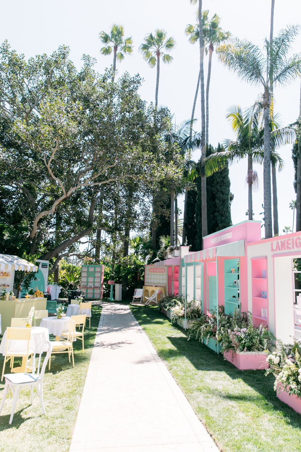 Panoramic view of colorful pastel beach cottages with palm trees lining a sandy pathway at a tropical resort.