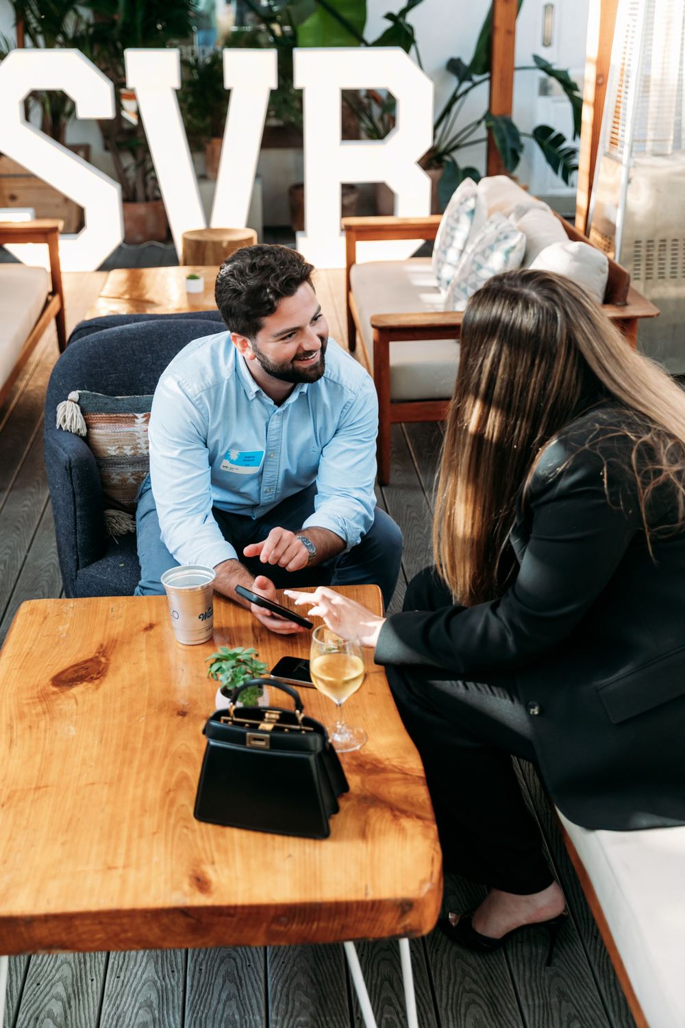 A couple having drinks and conversation at a rustic wooden restaurant table with wine glasses and casual attire.