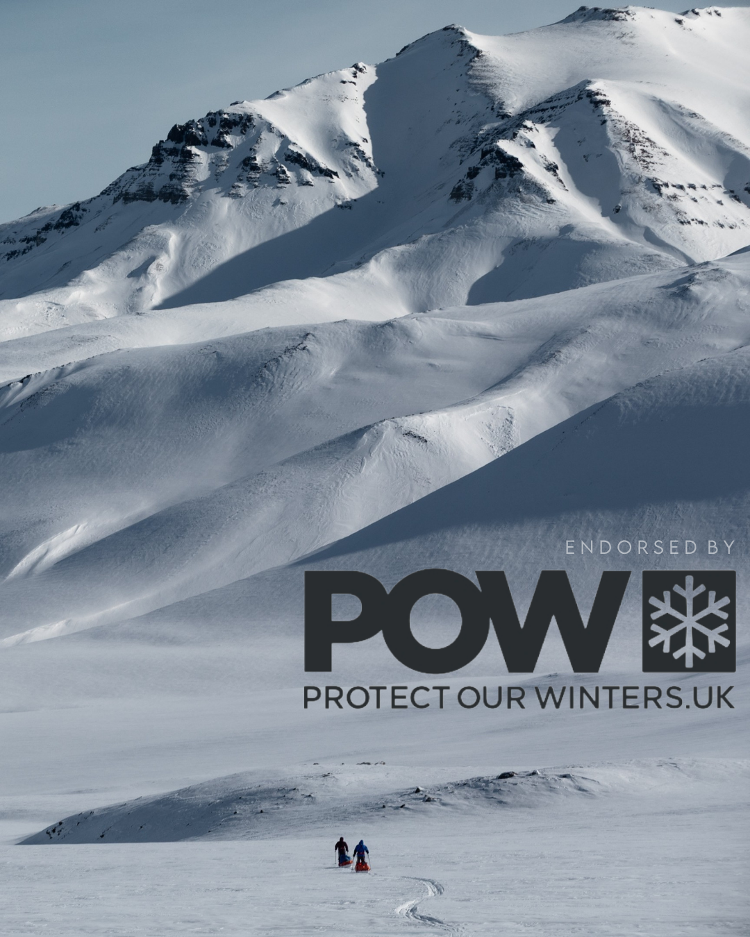 Snow-covered mountain peaks and ridges stretch across a dramatic winter landscape under cloudy skies.