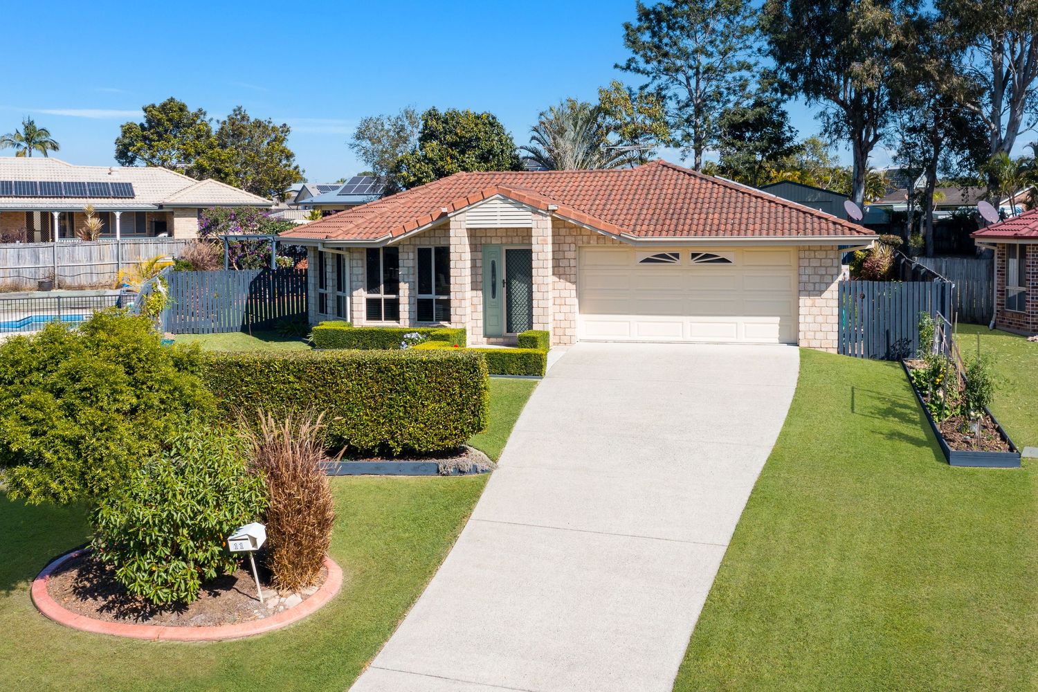 Neat brick home with terracotta roof, double garage, manicured lawn, and hedged garden in a quiet suburban street.