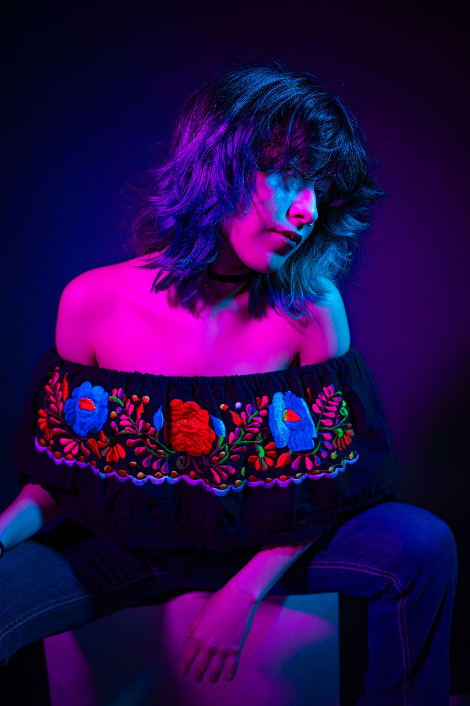 Artistic portrait series in neon pink and blue lighting showing shoulders with embroidered floral details on dark fabric.