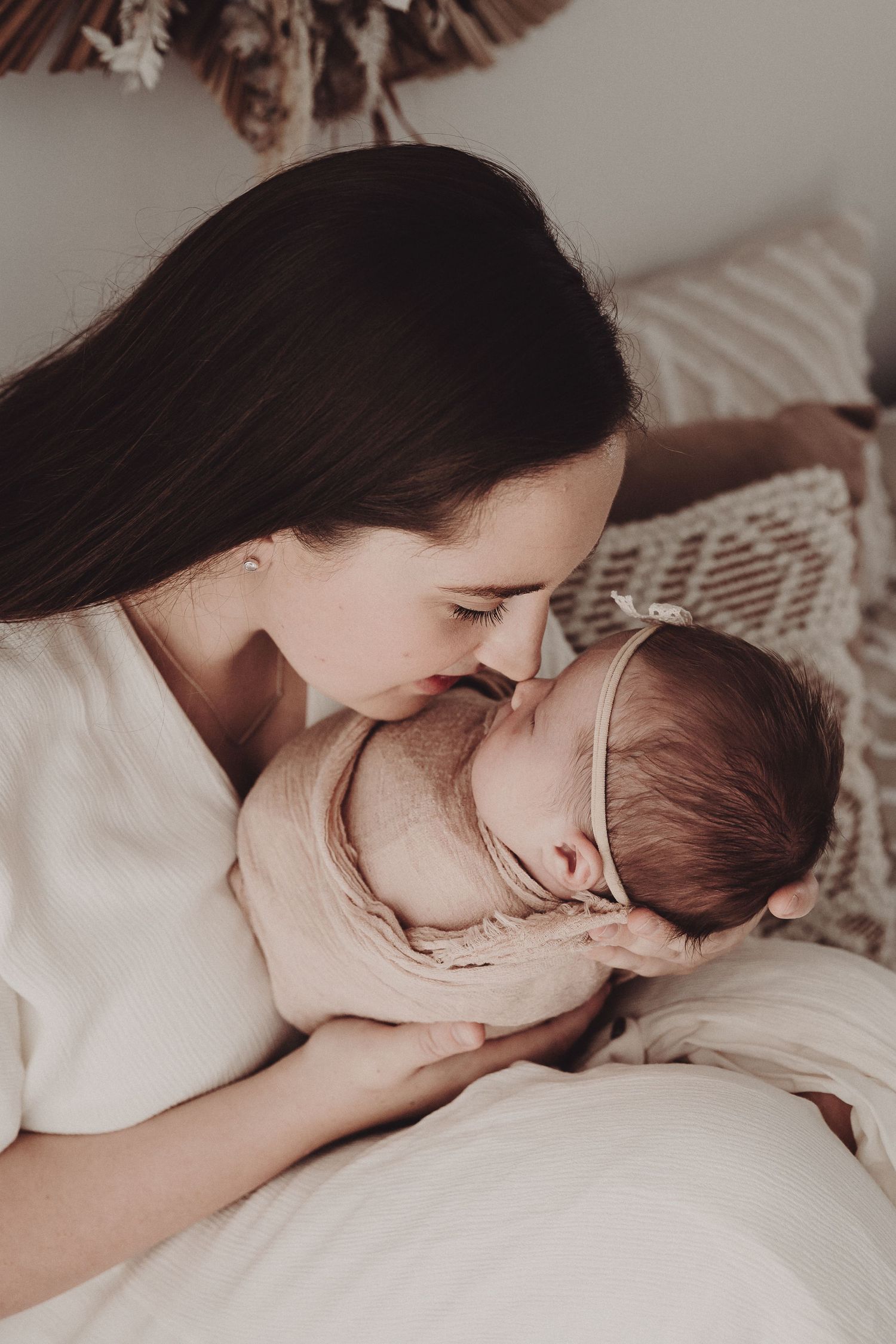 Tender moments captured in a series of intimate black and white photographs showing parent and baby bonding on white bedding.