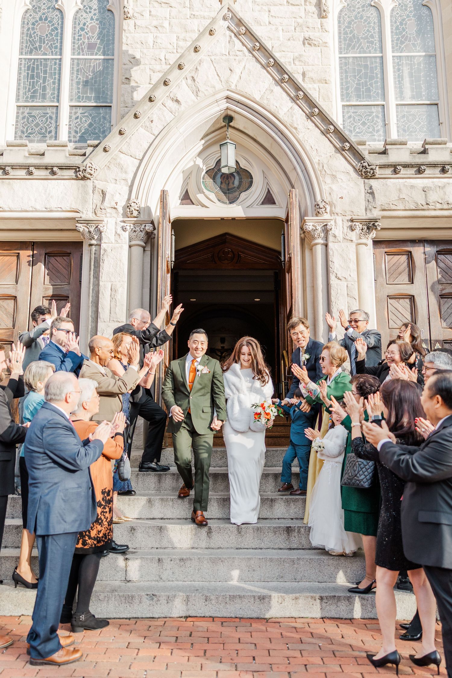 Wedding guests line up outside a historic stone church to celebrate as newlyweds exit after their ceremony.