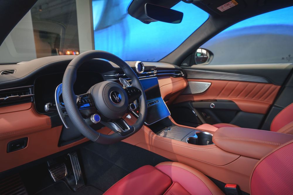 Luxury car interior with red leather seats and modern dashboard illuminated by blue ambient lighting.