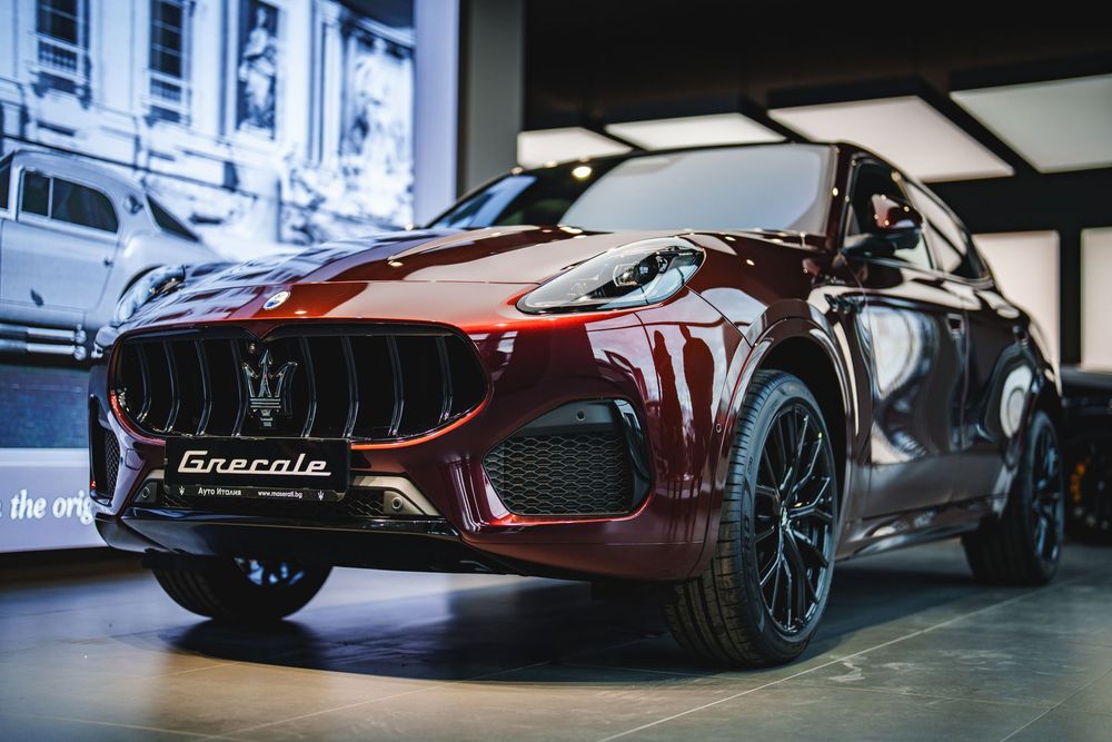 A sleek red Maserati luxury sports car displayed in a modern showroom with dramatic lighting and reflective floors.
