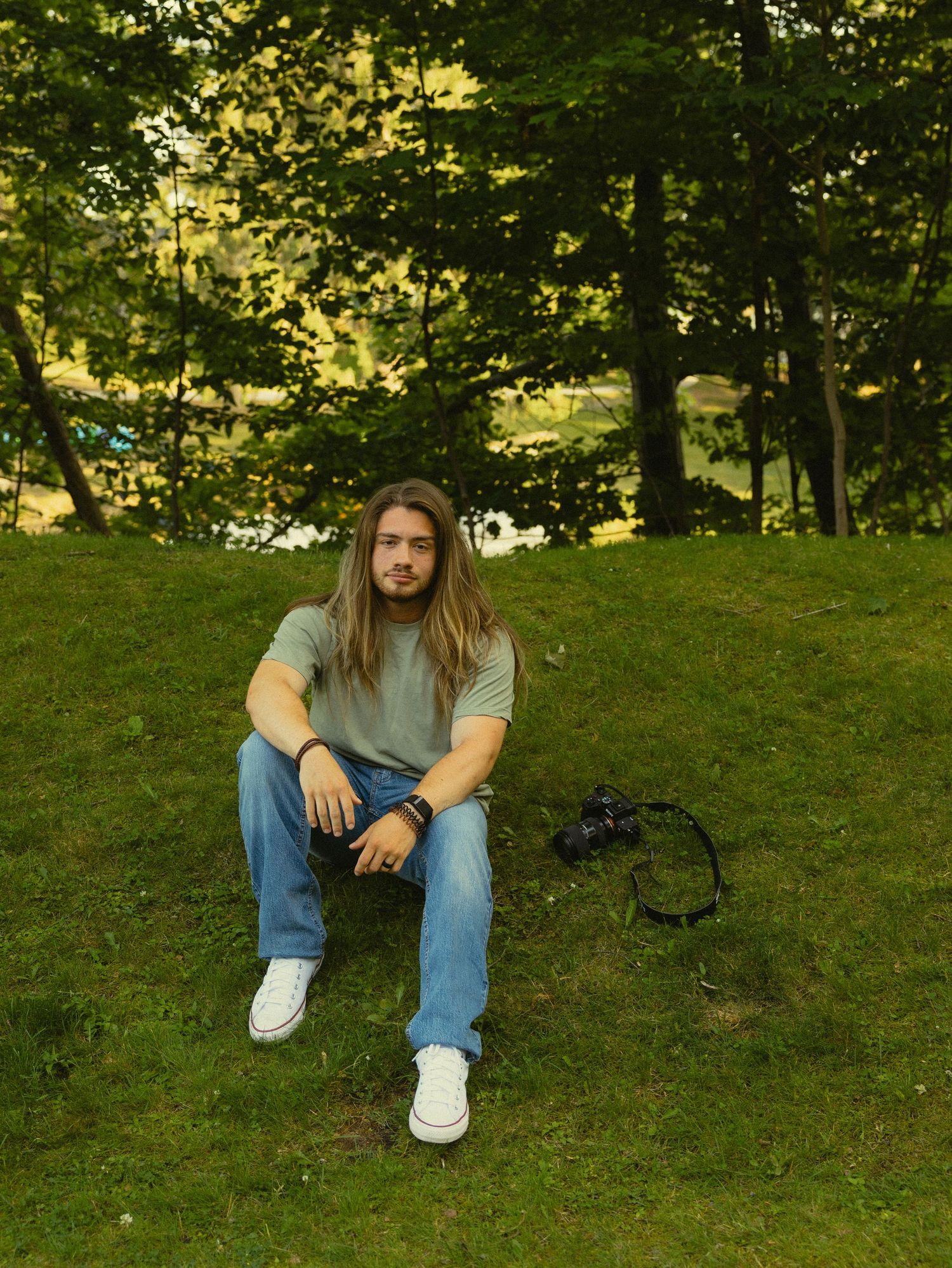 Someone wearing a white t-shirt stands in a green field under cloudy skies on a summer day.