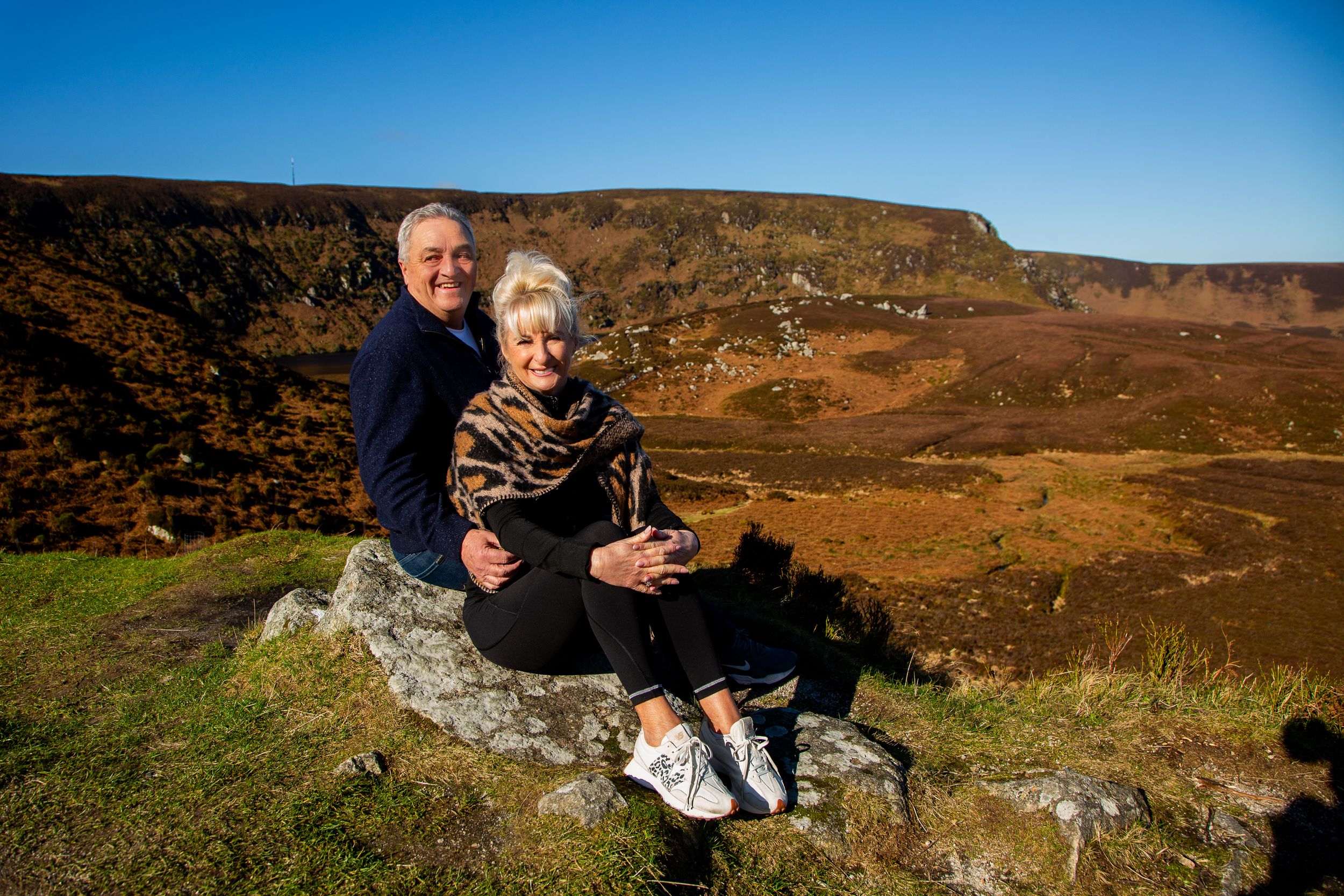 couple photography on boulder in wicklow countryside overlooking dramatic mountain scenery.