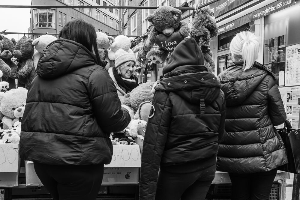 Black and white photo of people wearing winter coats gathered at an outdoor market or vendor stall.