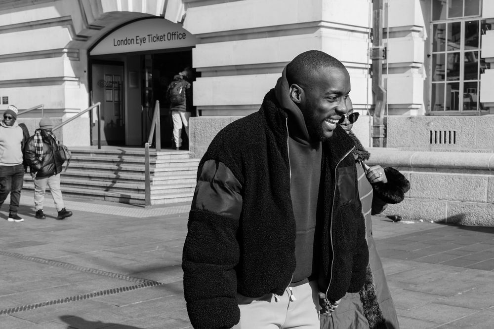 A sequence of black and white photos shows a person in a dark coat walking and gesturing outside a building.