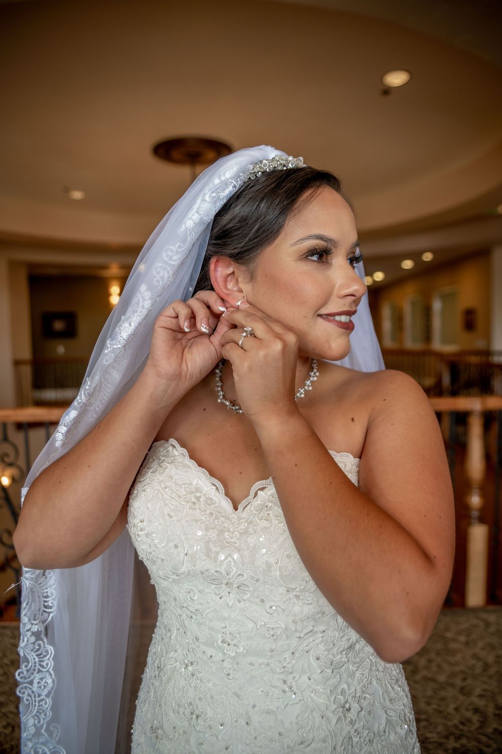 Bride in a white lace wedding dress and veil adjusts her earring in a sequence of elegant getting ready photos.