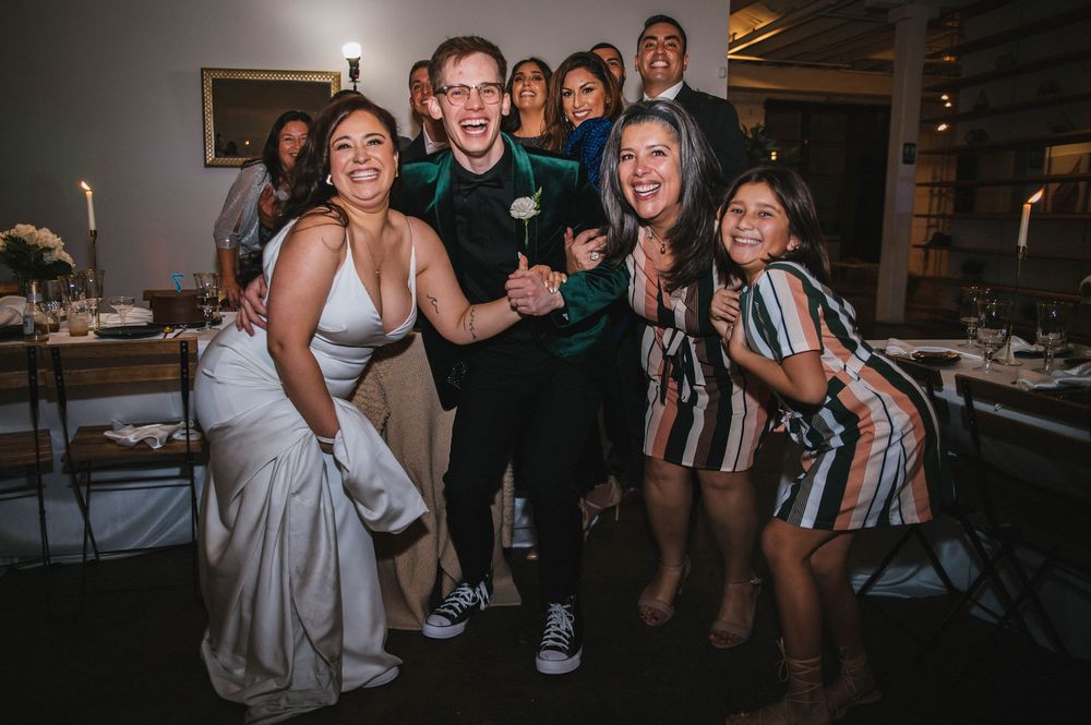 A group of wedding guests dancing and celebrating together at a reception party in an indoor venue.