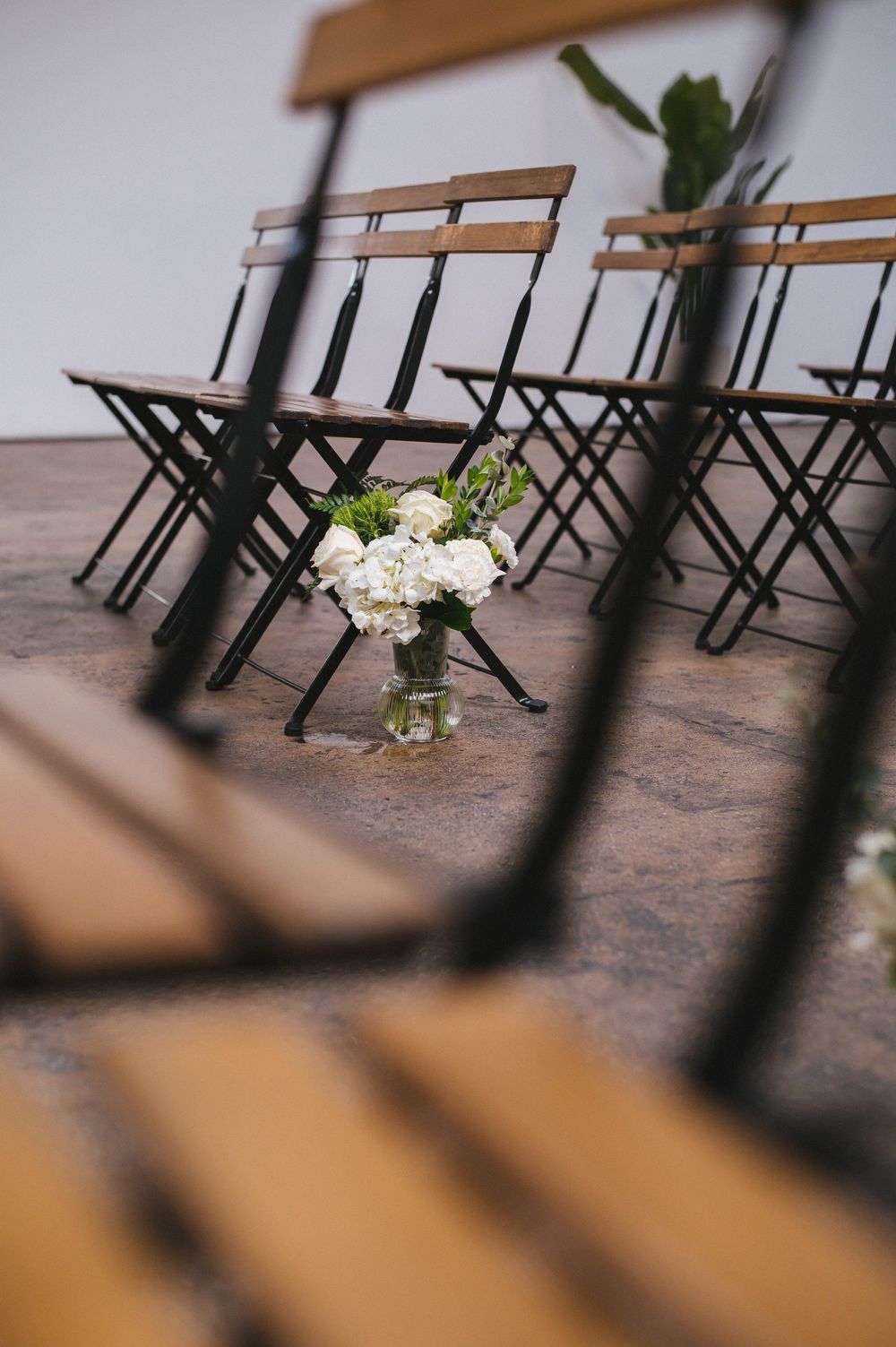 Wooden benches arranged in rows with a small floral centerpiece vase creating an intimate indoor ceremony setting.