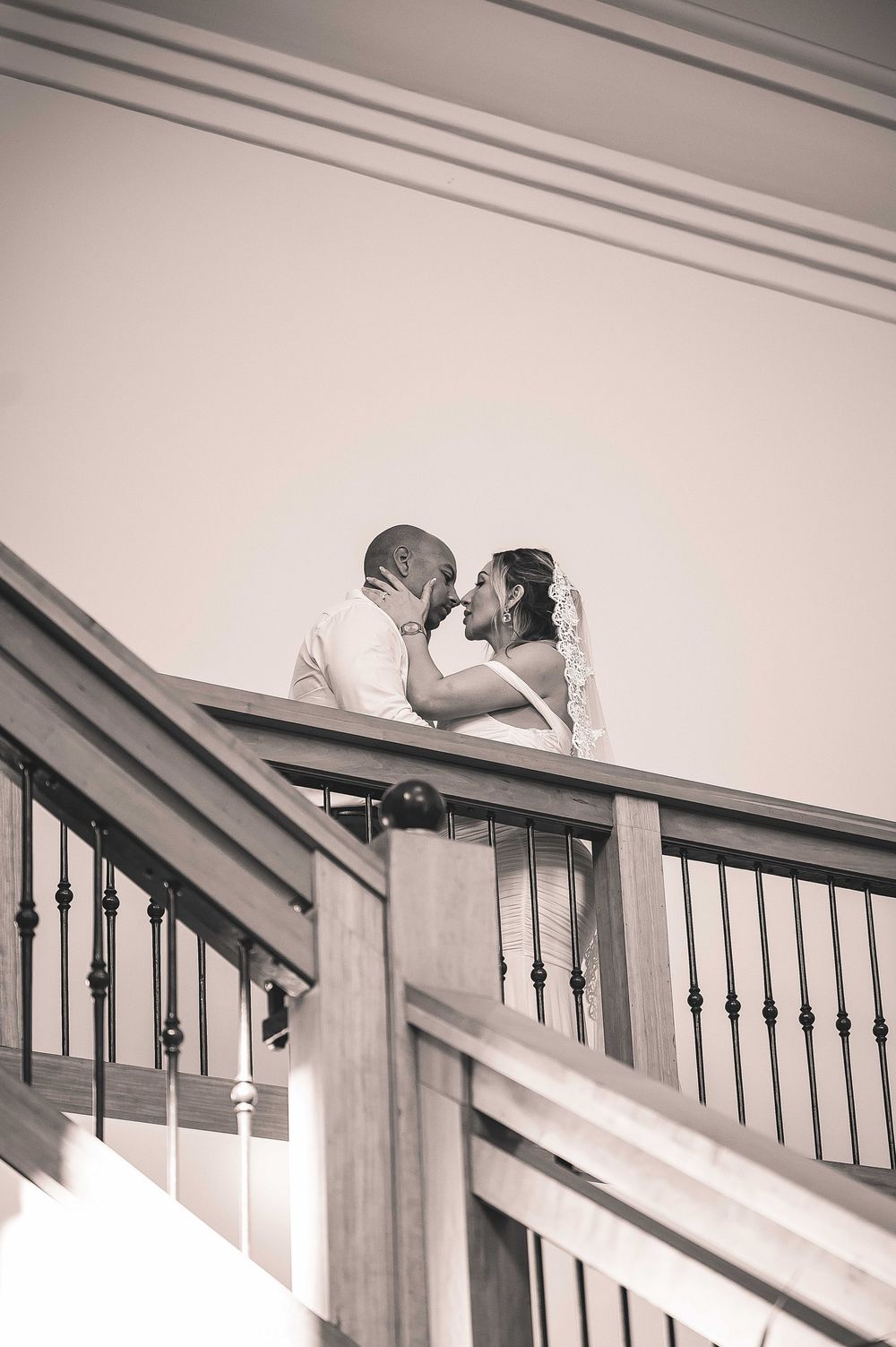 A romantic black and white moment captured on an elegant wooden staircase with decorative balusters.